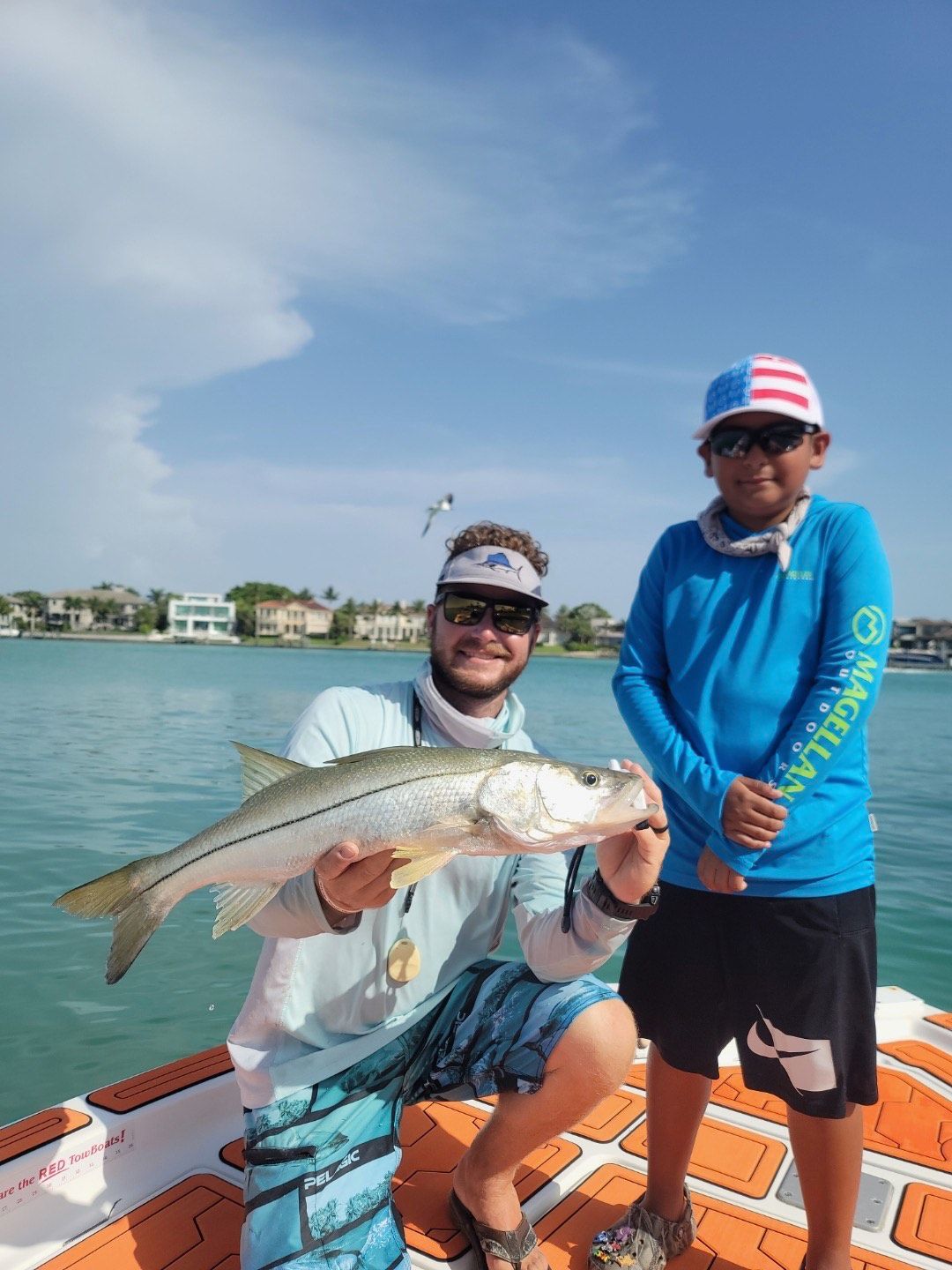 Two people on a boat with a caught fish, against a blue sky and water.