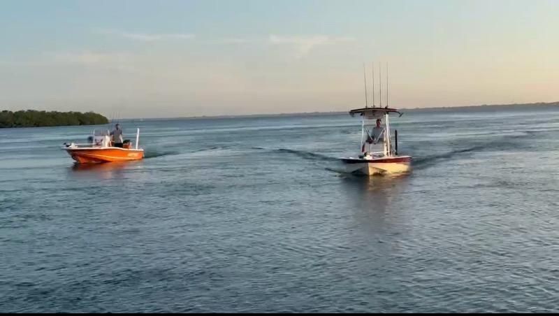 Two boats on blue water, one orange and one white with fishing rods.