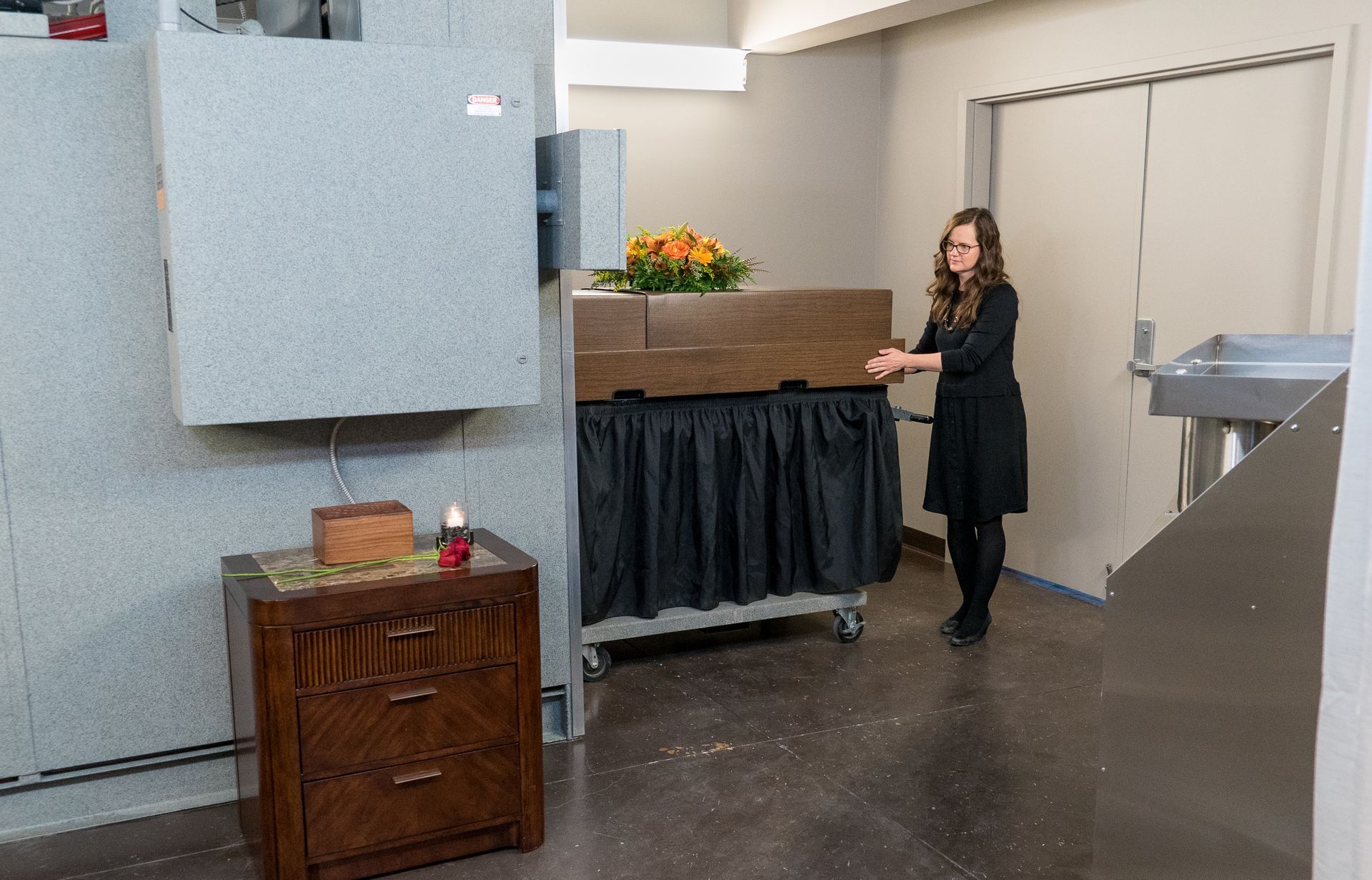 A woman is standing next to a coffin in a room.