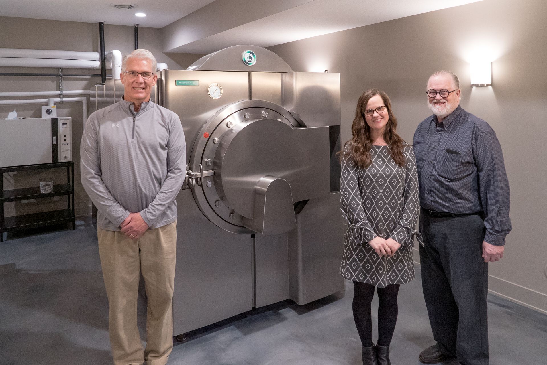 Three people are standing in front of a large machine in a room.