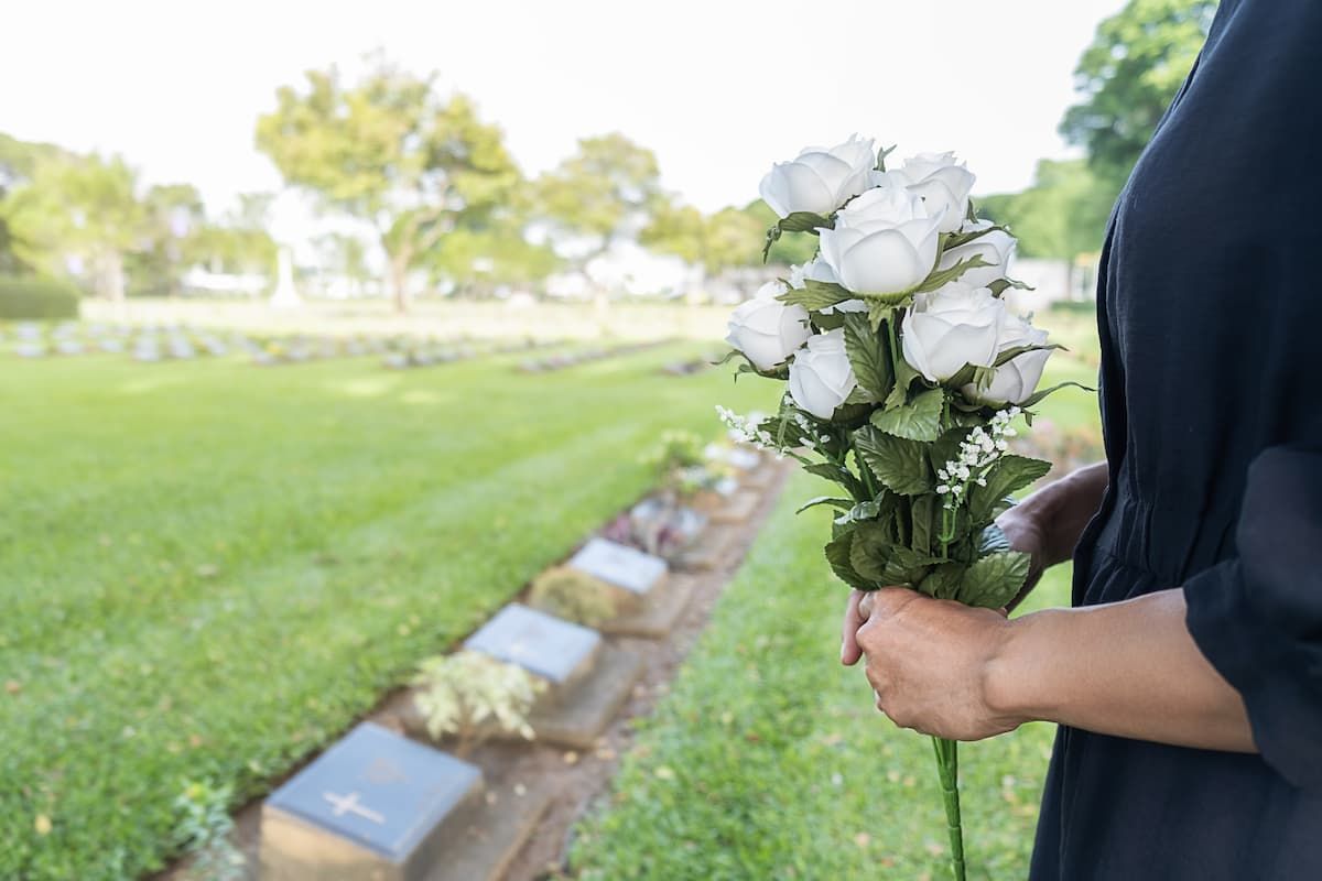 A woman is holding a bouquet of white roses in a cemetery.