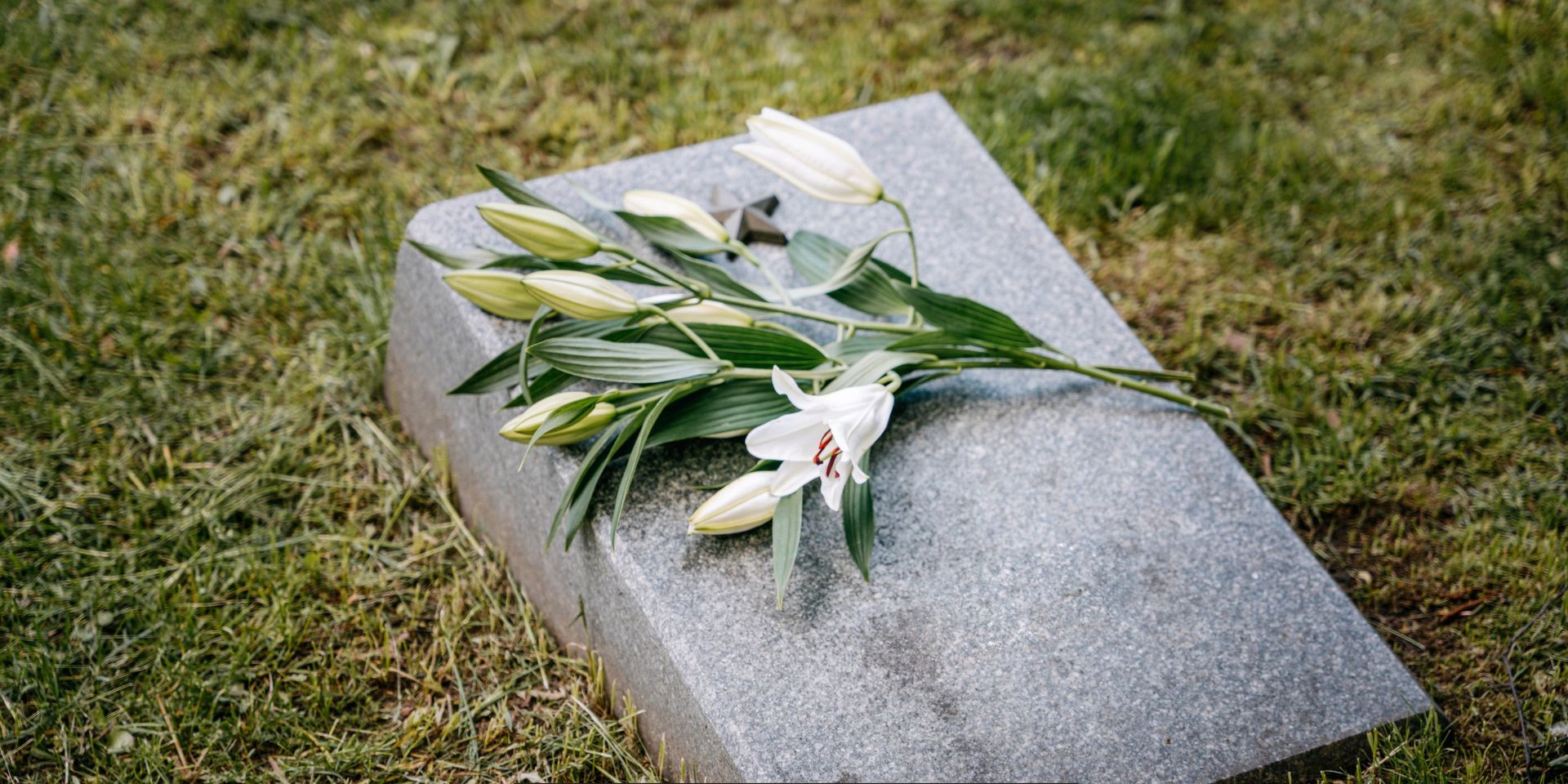 White lilies resting on a granite gravestone, symbolizing remembrance and honoring a loved one at a memorial site