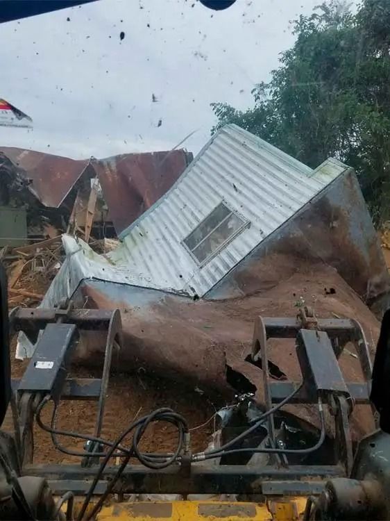 Tornado aftermath with a collapsed white house, debris, and an overturned vehicle under a stormy sky