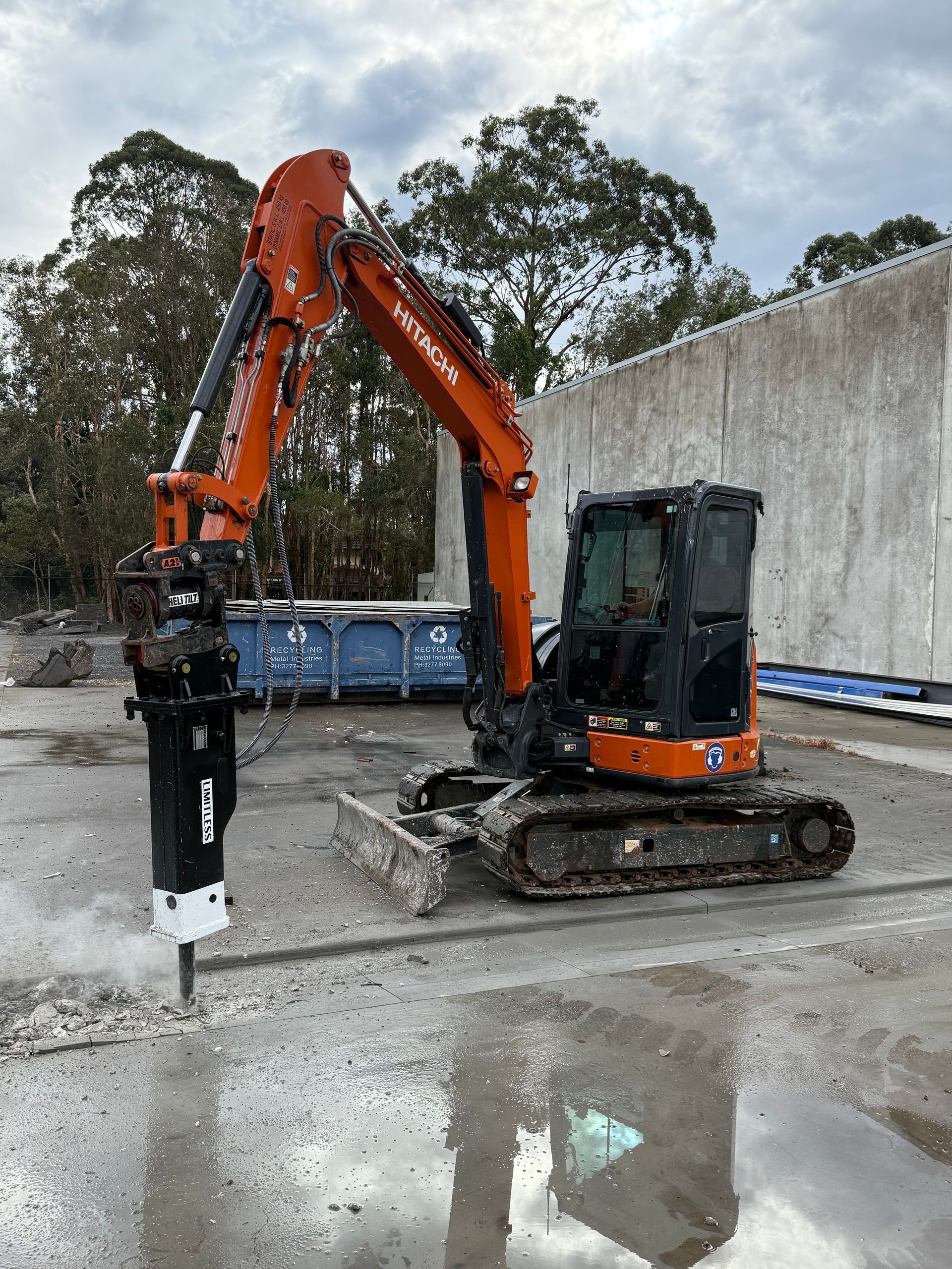 Orange excavator with jackhammer attachment on a wet concrete surface.