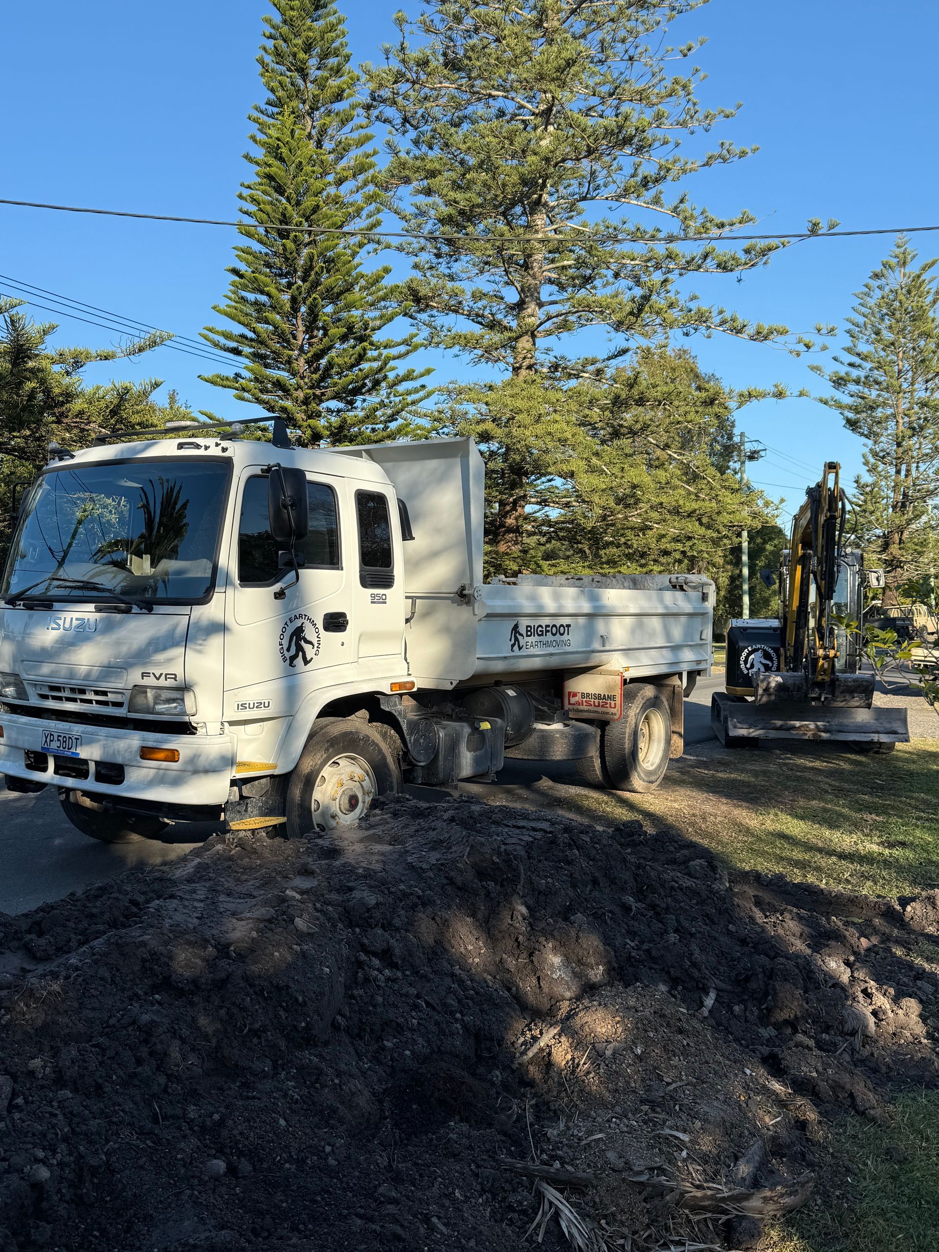 White truck parked on a dark dirt pile next to an excavator; sunny outdoor setting.
