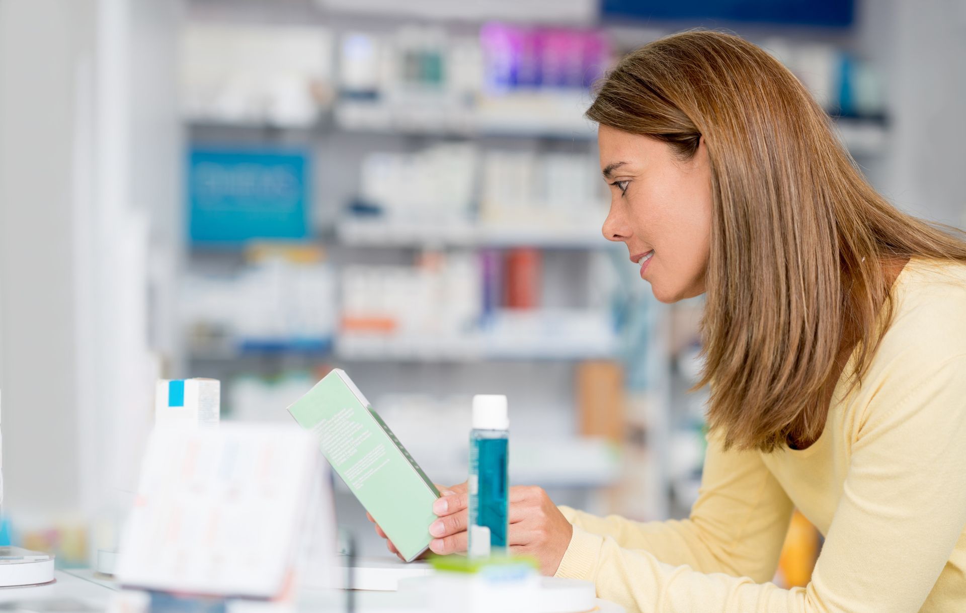 Una donna è seduta alla scrivania di una farmacia e legge un libro.