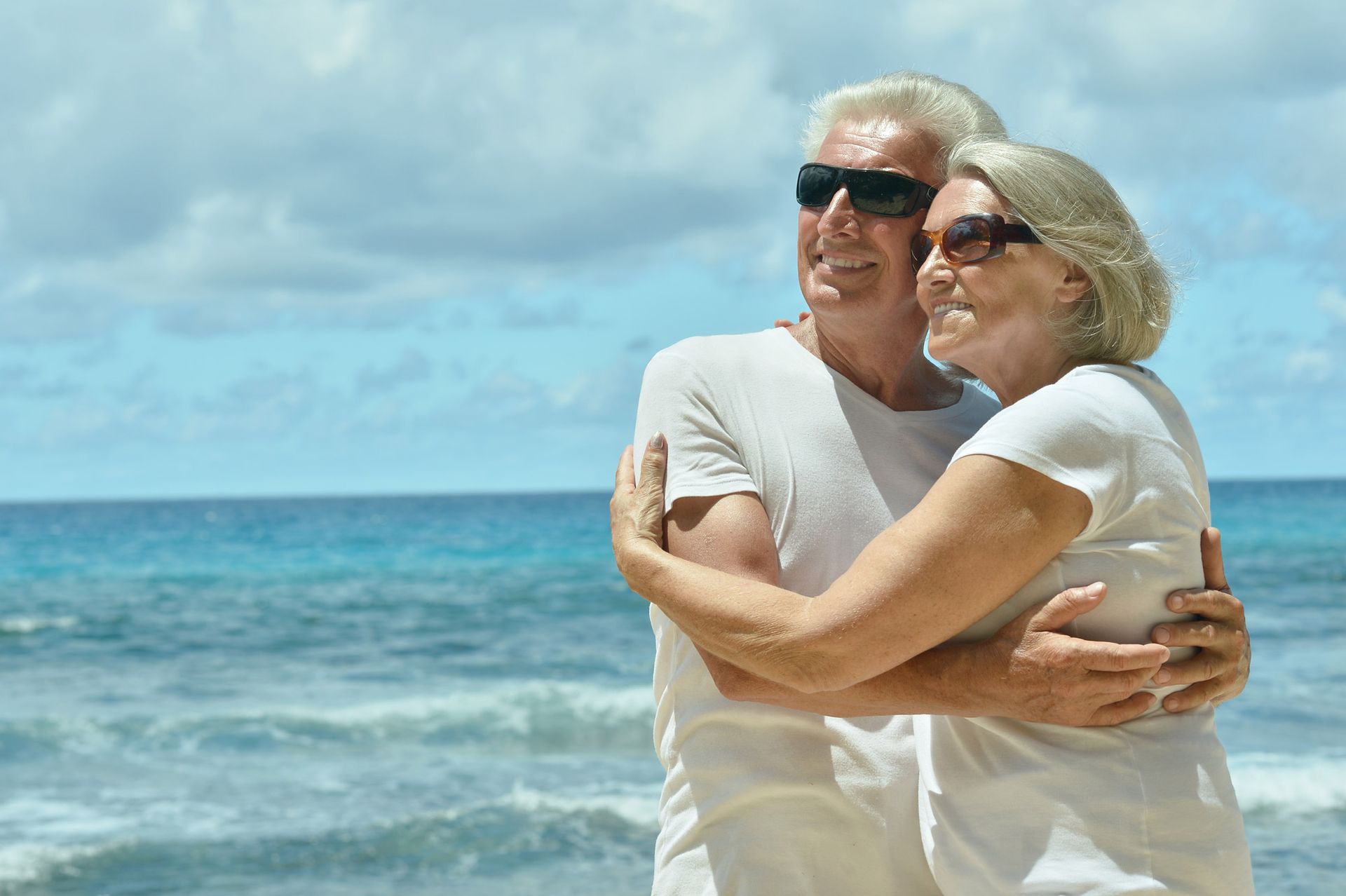 An elderly couple is hugging each other on the beach.