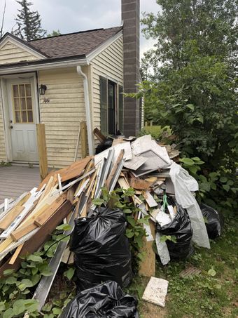 A dumpster is parked on the side of the road in front of a house.