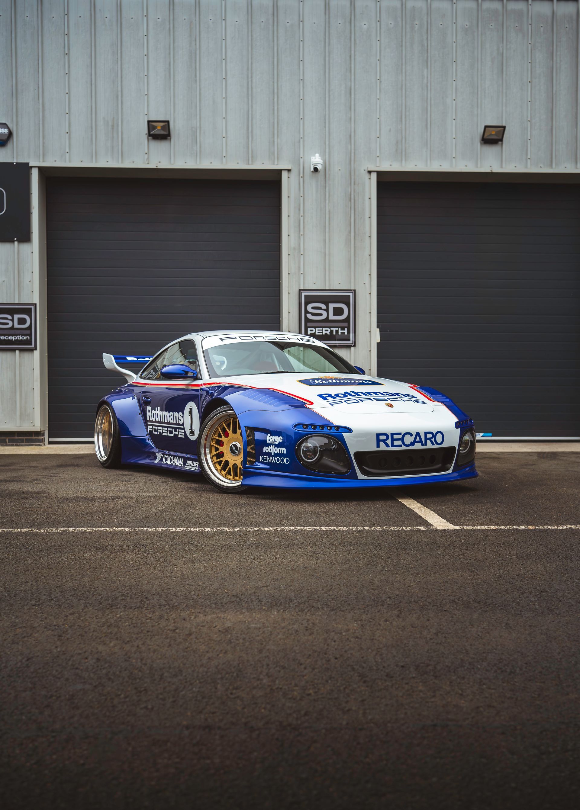 A blue and white sports car is parked in front of a garage.