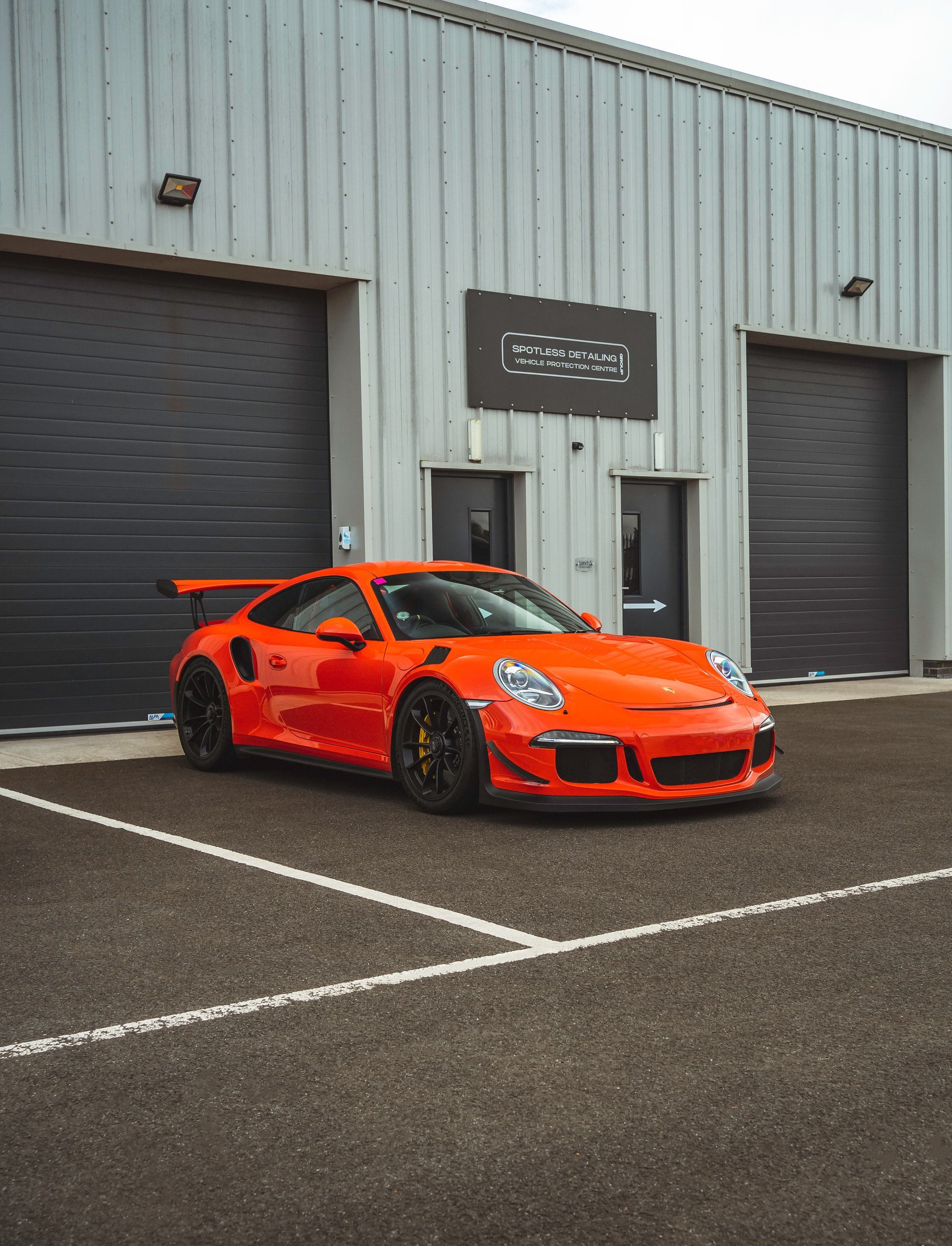 An orange porsche 911 gt3 rs is parked in a parking lot in front of a building.