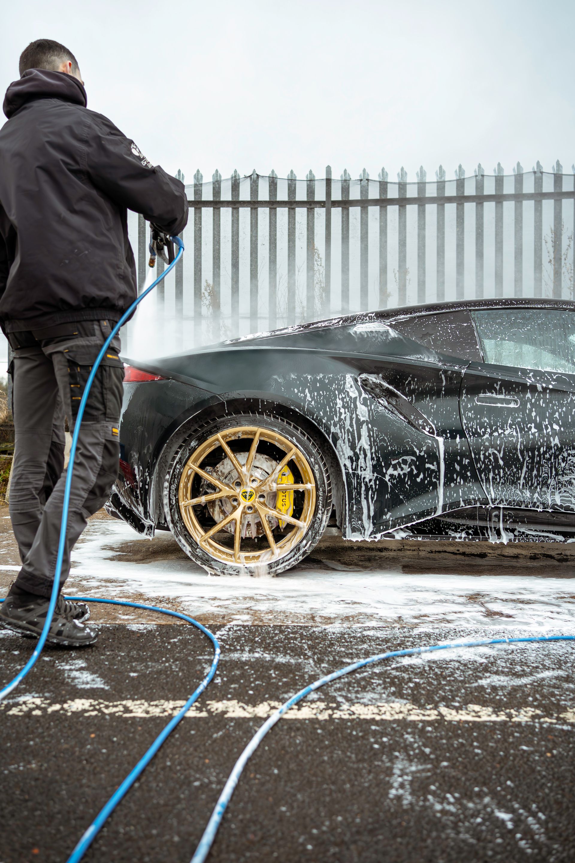 A man is washing a black sports car with a hose.