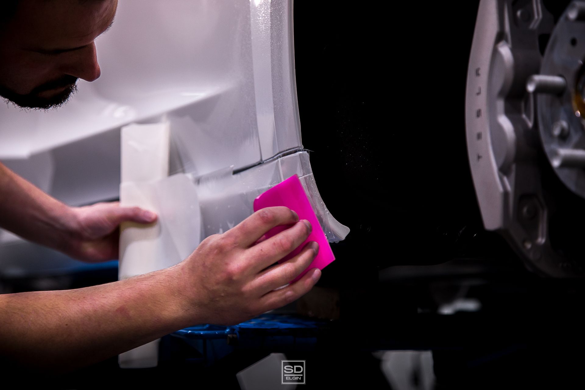 A man is wrapping a car with tape and a pink sponge.