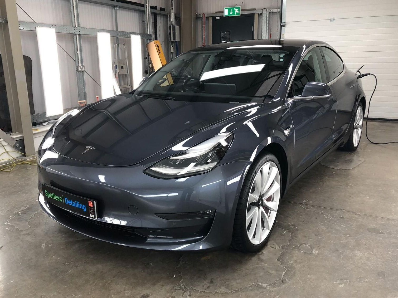A tesla model 3 is being charged in a garage.