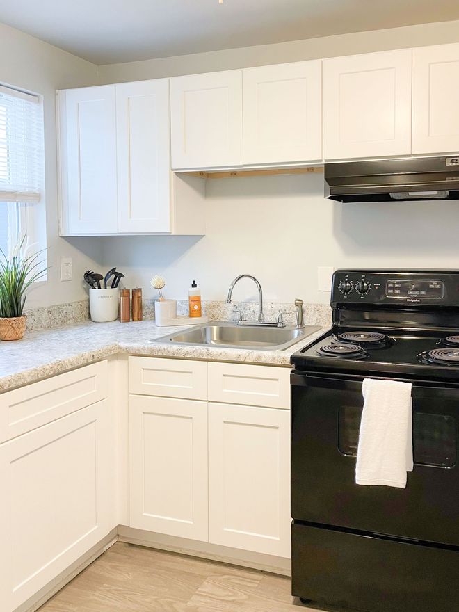 A kitchen with white cabinets , a black stove , a sink , and a window.