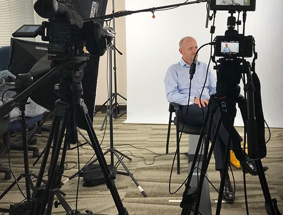 Interview setup with cameras on tripods filming a seated man in a studio