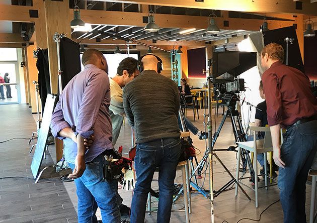 People setting up camera tripods in a studio with bright lights and equipment