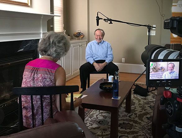 Interview setup with two seated people in a living room, filmed by a camera on a tripod.