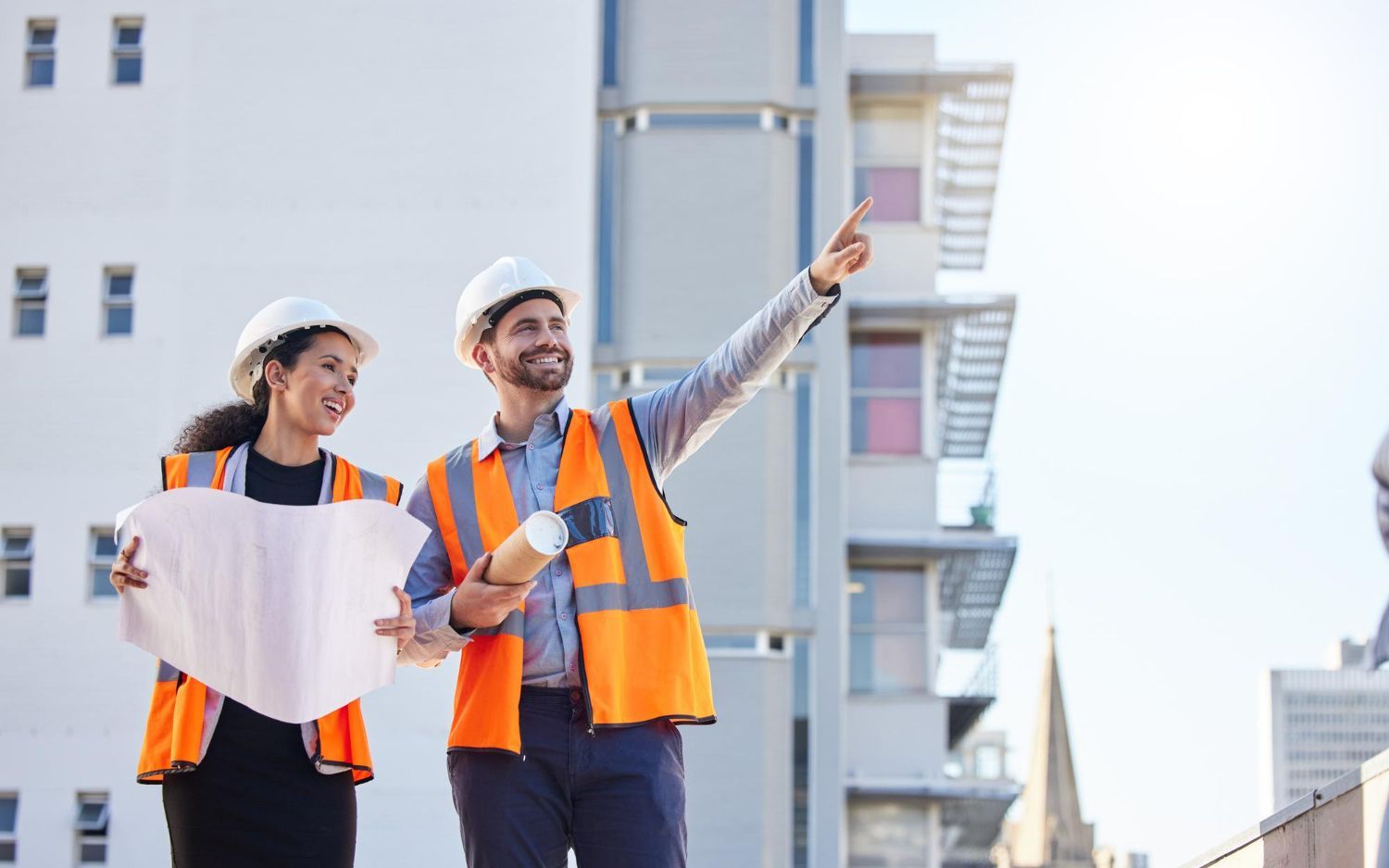 Couple in a convertible car, smiling while driving through a green, wooded area on a sunny day.
