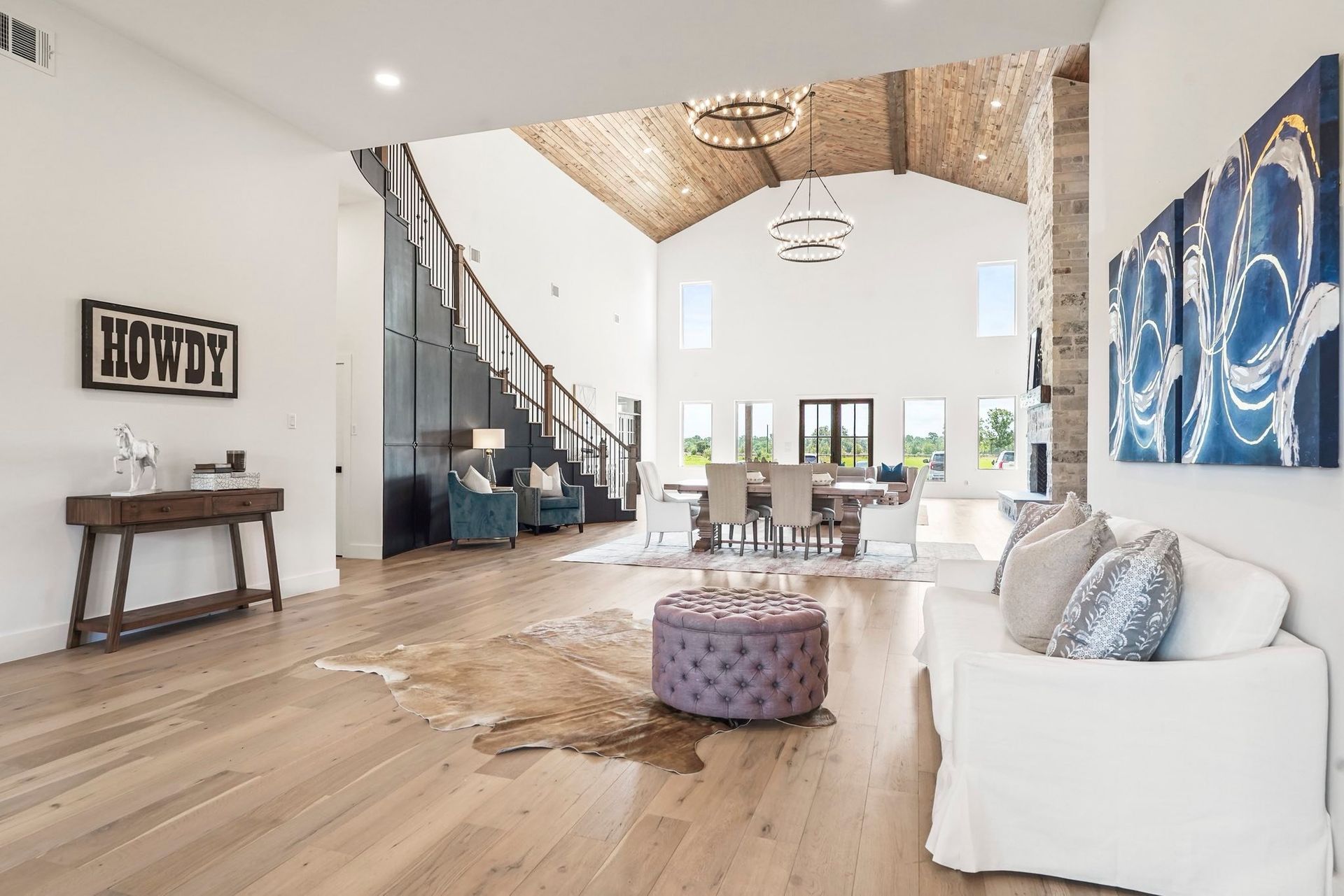 Spacious living room with wood floors, a staircase, and a dining area, featuring a cowhide rug and artwork. Spacious living room with wood floors, a staircase, and a dining area, featuring a cowhide rug and artwork.