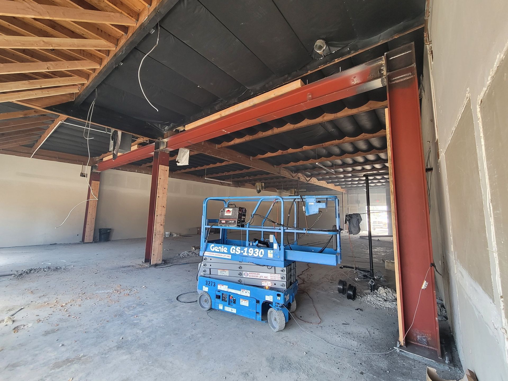 A blue scissor lift is sitting inside of a building under construction.