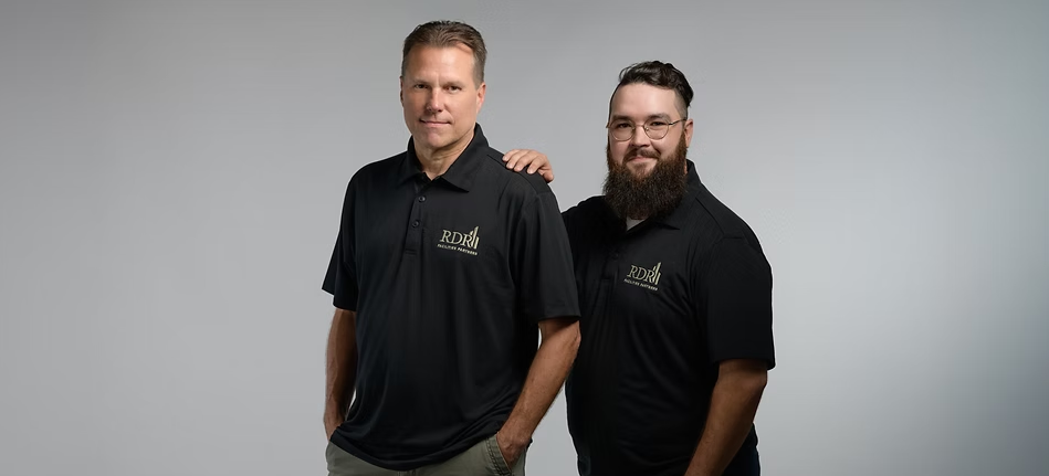 Two men in black polo shirts standing against a light gray background