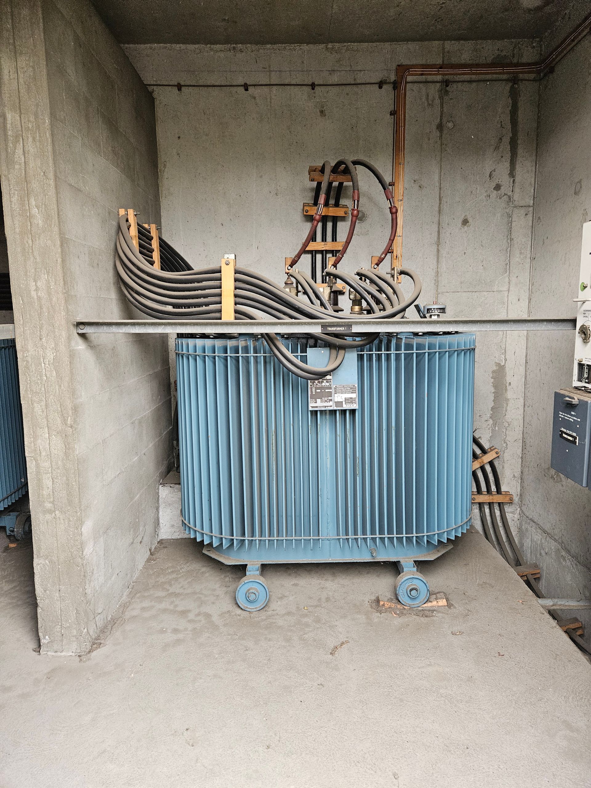 En blå transformer står oven på et betongulv i et rum.