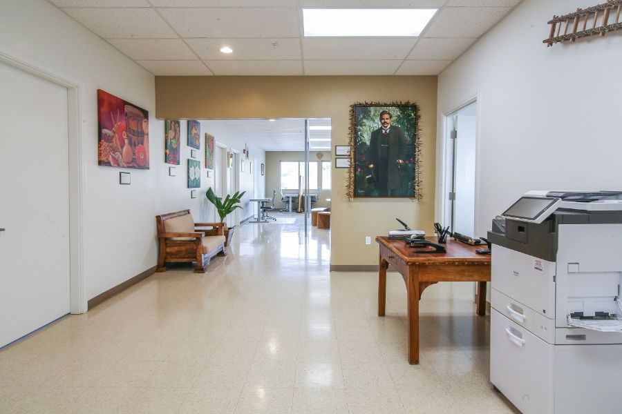 A hallway with a desk , printer , and a painting on the wall.