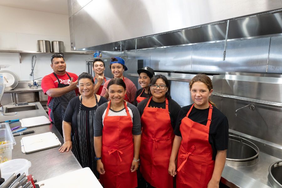 a group of people wearing red aprons are posing for a picture in a kitchen.