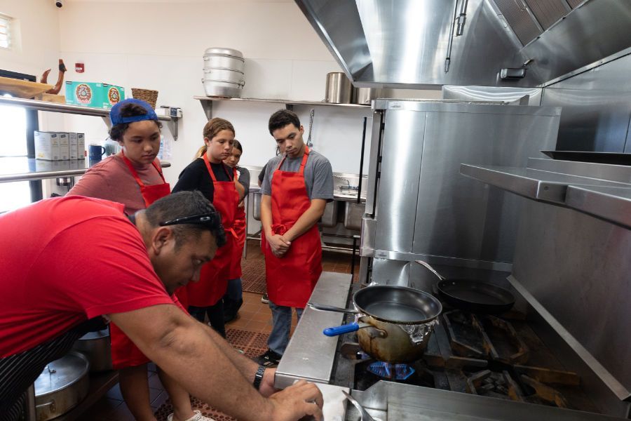 a group of people are standing around a stove in a kitchen .