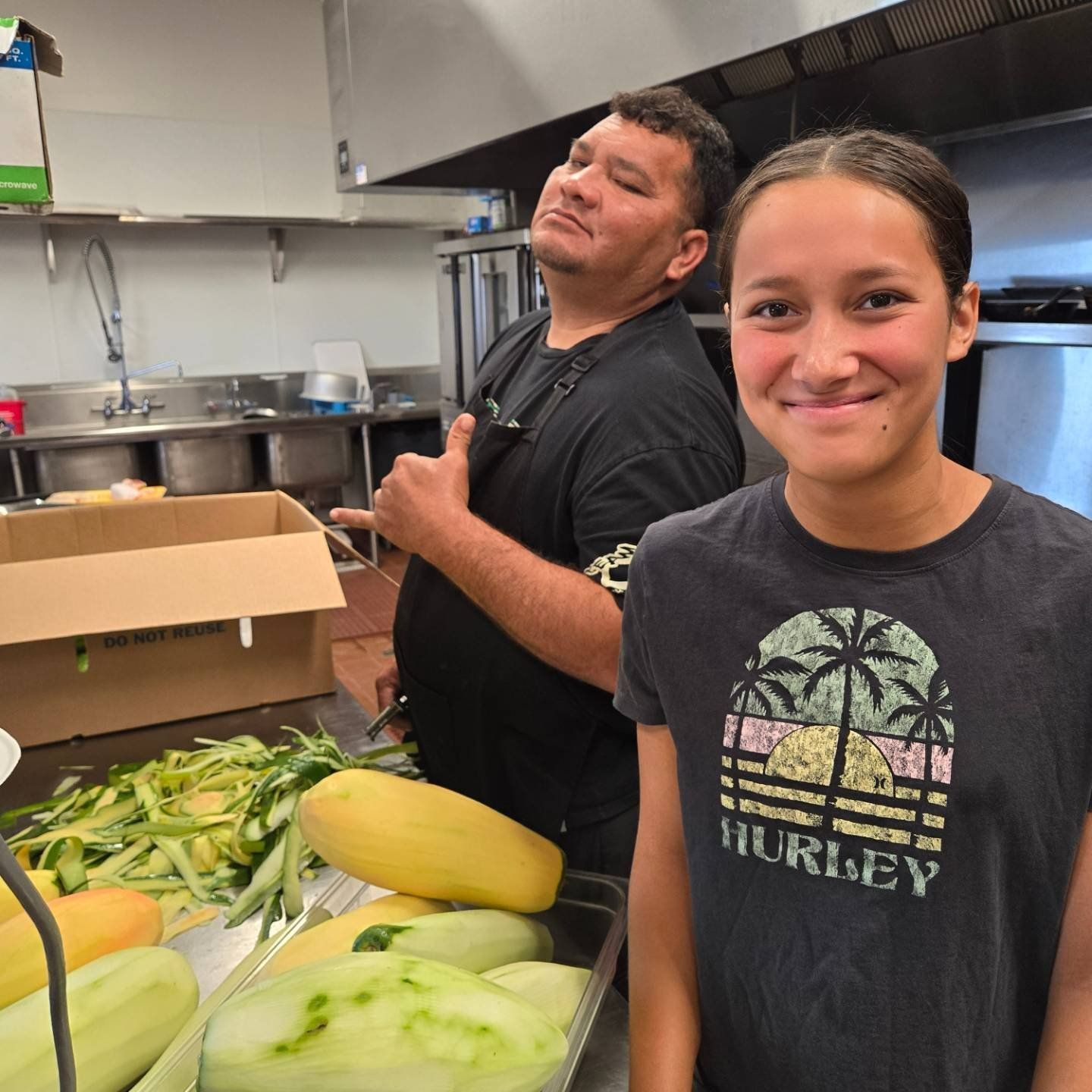 A woman wearing a hurley shirt stands next to a man in a kitchen