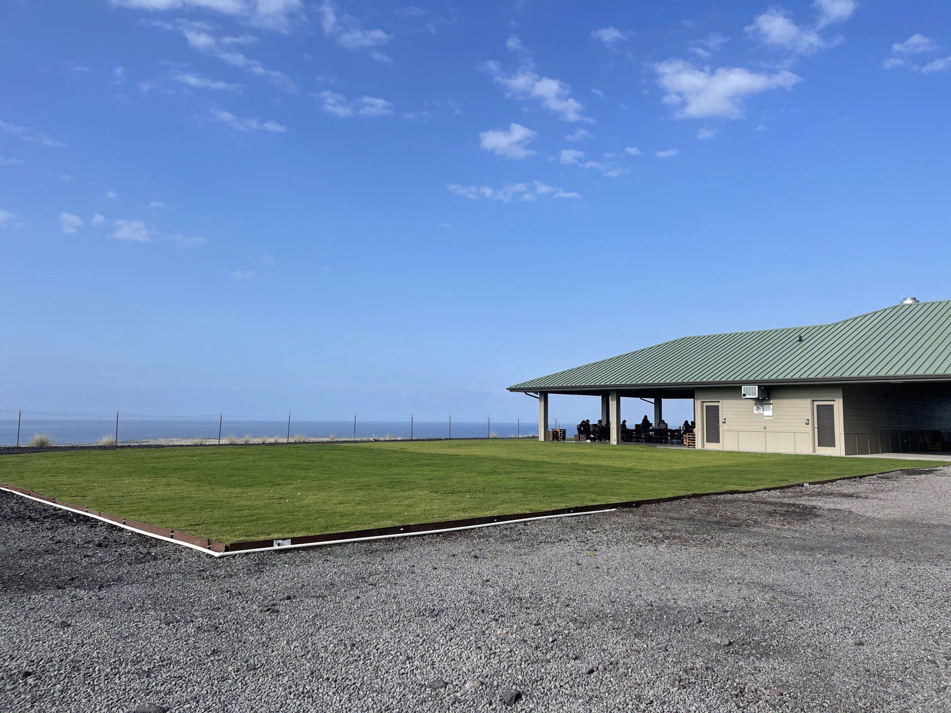 A house with a green roof is sitting on top of a lush green field.