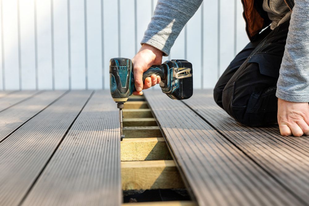 A Man Is Installing A Wooden Deck With A Drill — Corbett Brothers Flooring In Woy Woy, NSW