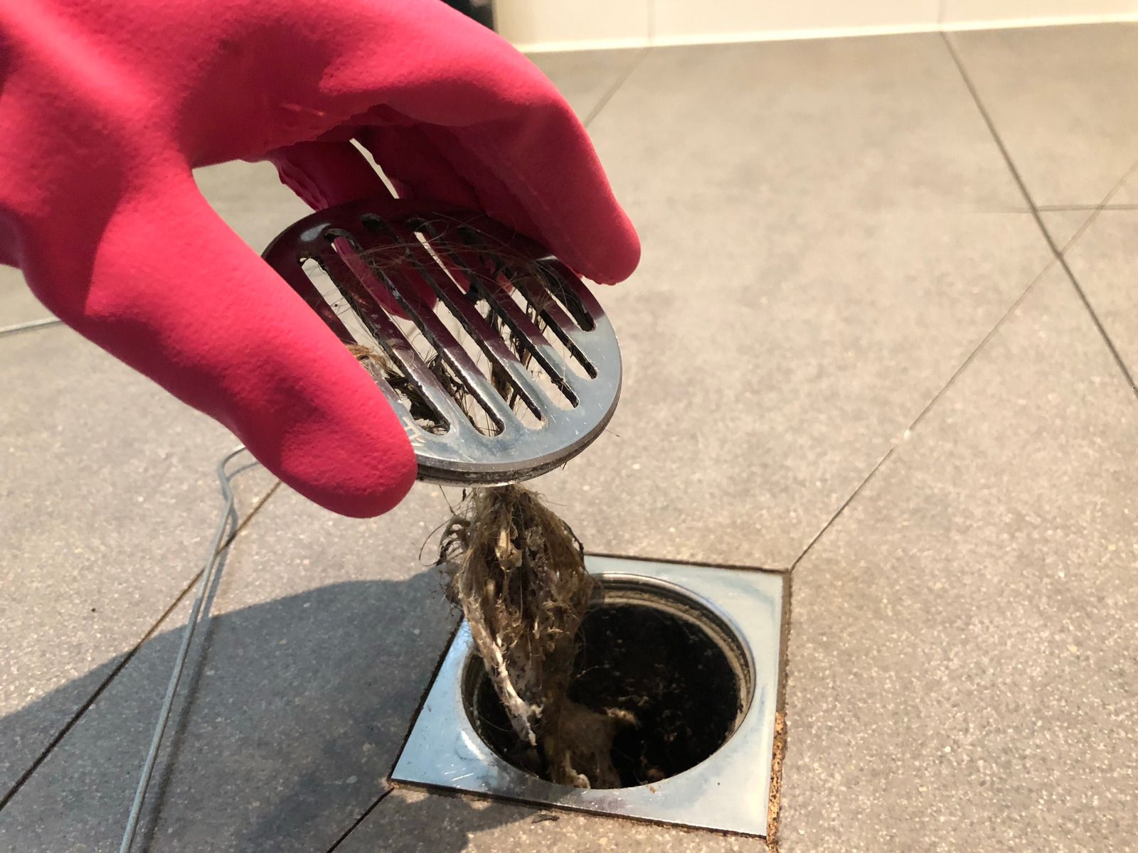 A person wearing a red rubber glove is cleaning a drain.