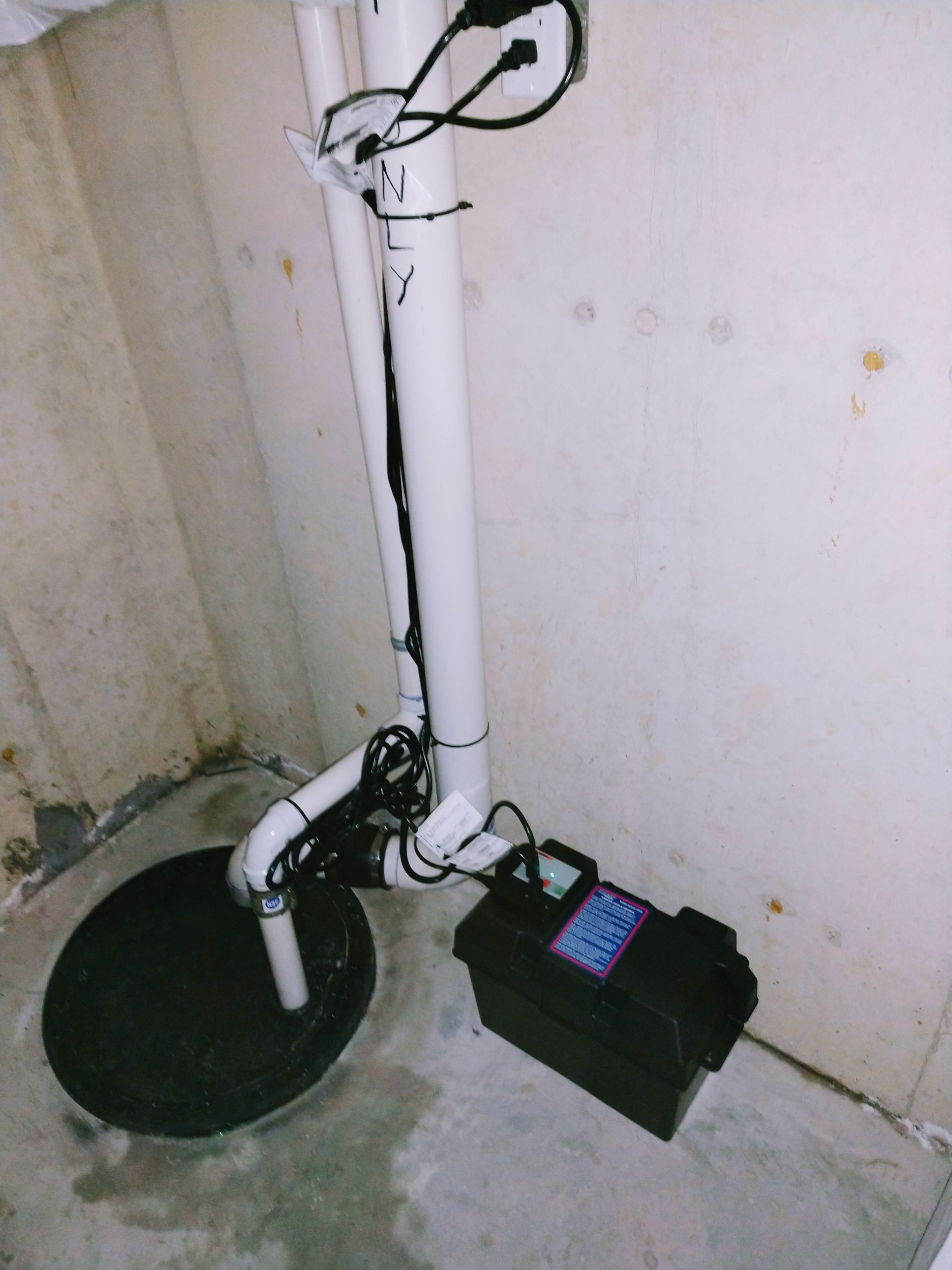 A white pipe is connected to a black box in a basement