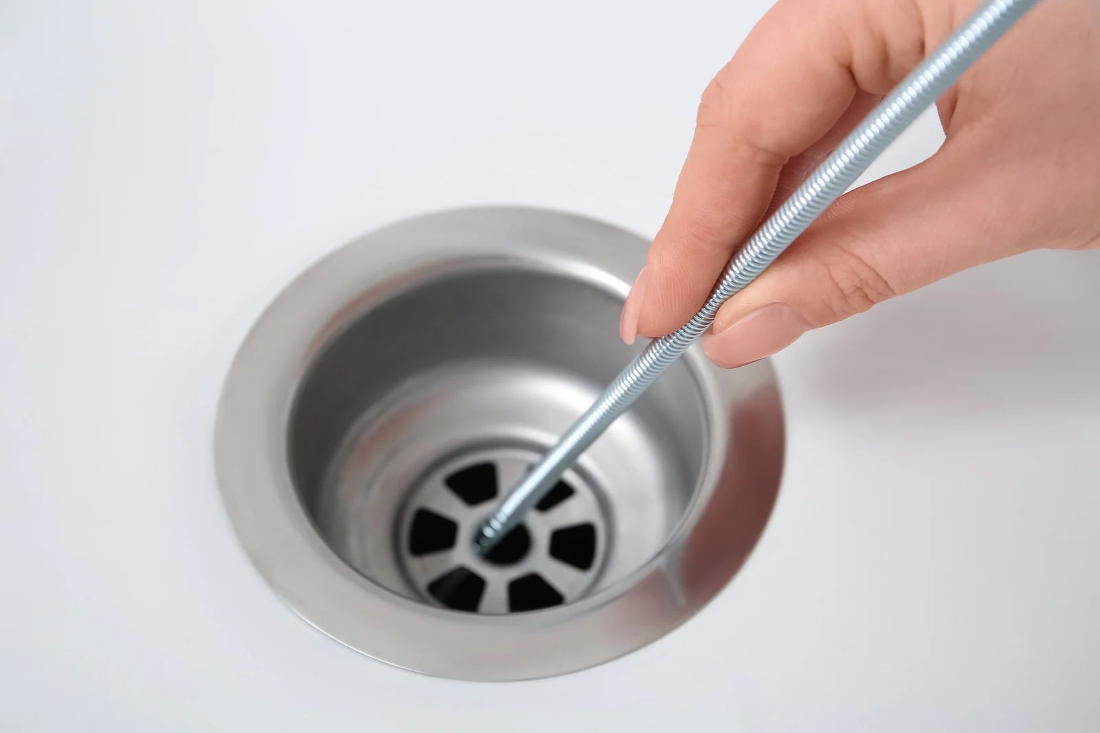 Hand with drain snake cleaning a white sink drain.