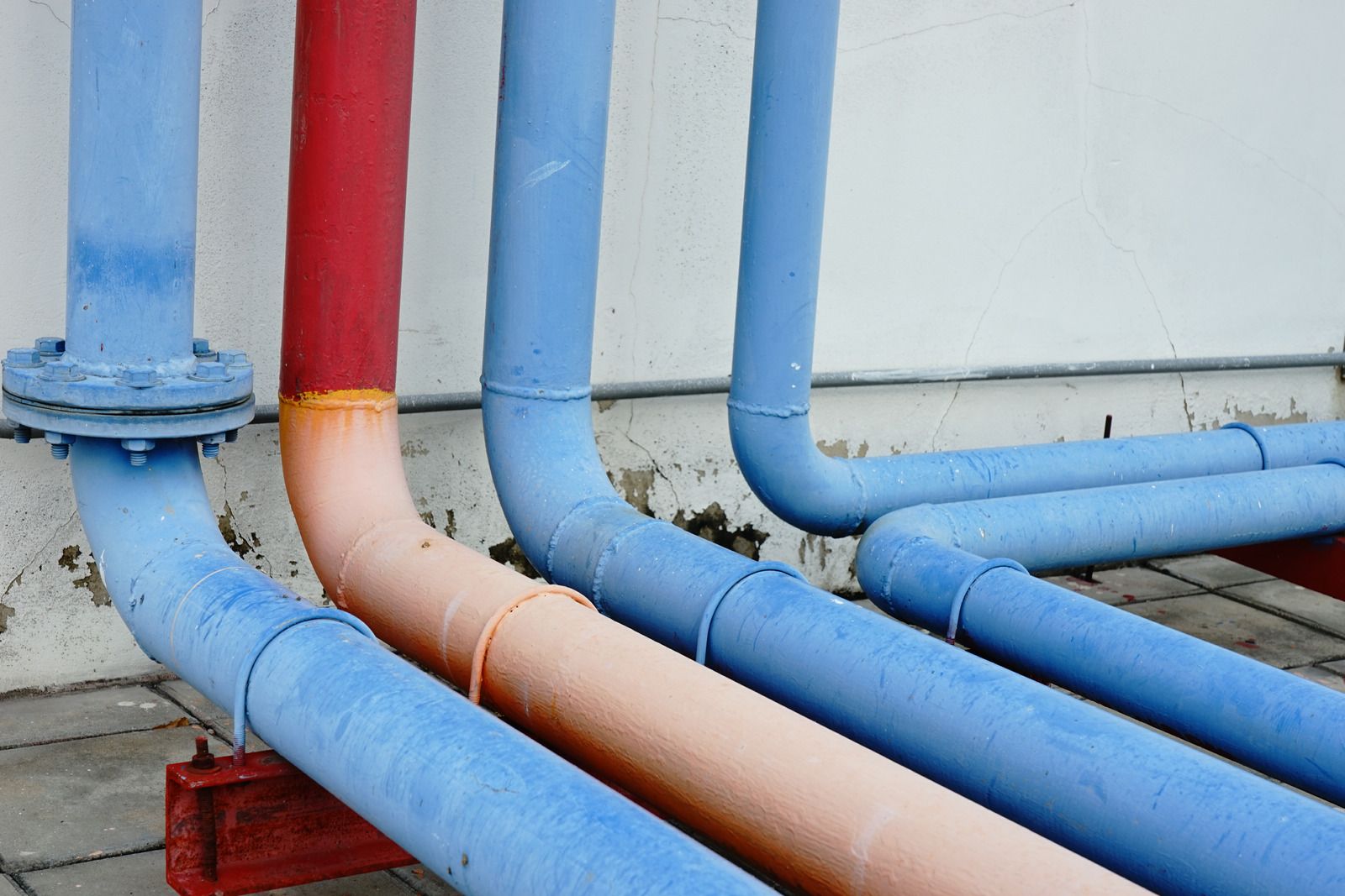 Blue and red painted pipes on a white wall, with metal supports.