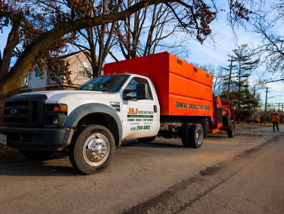 Orange utility truck parked on a roadside with trees and workers in the background