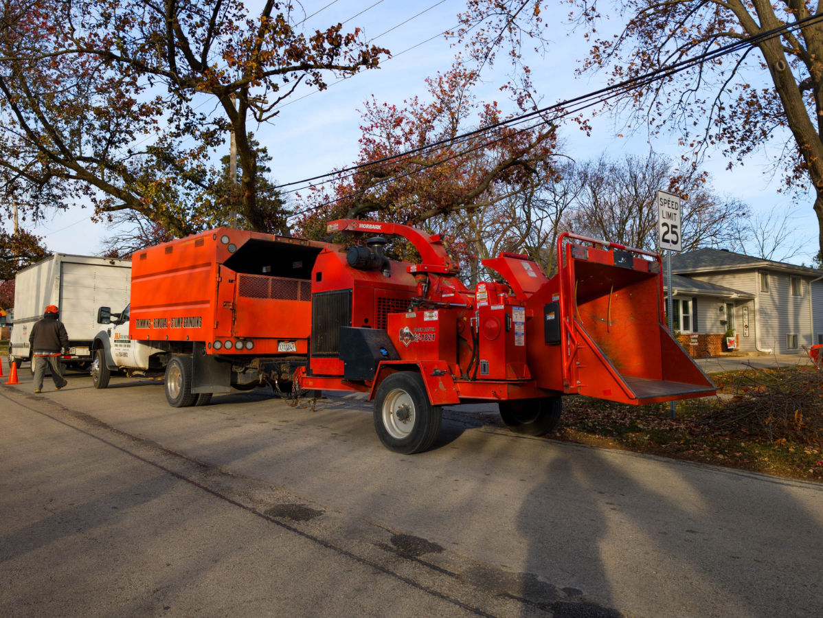Bright orange wood chipper truck parked on a residential street with workers nearby