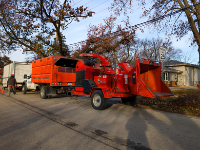Bright orange wood chipper truck parked on a residential street with workers nearby