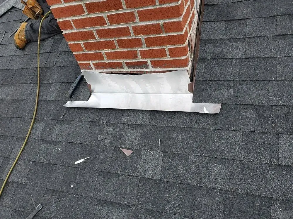 Brick chimney with silver flashing on a dark shingle roof.