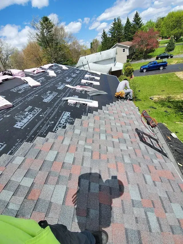 Roofers installing shingles on a house roof on a sunny day.