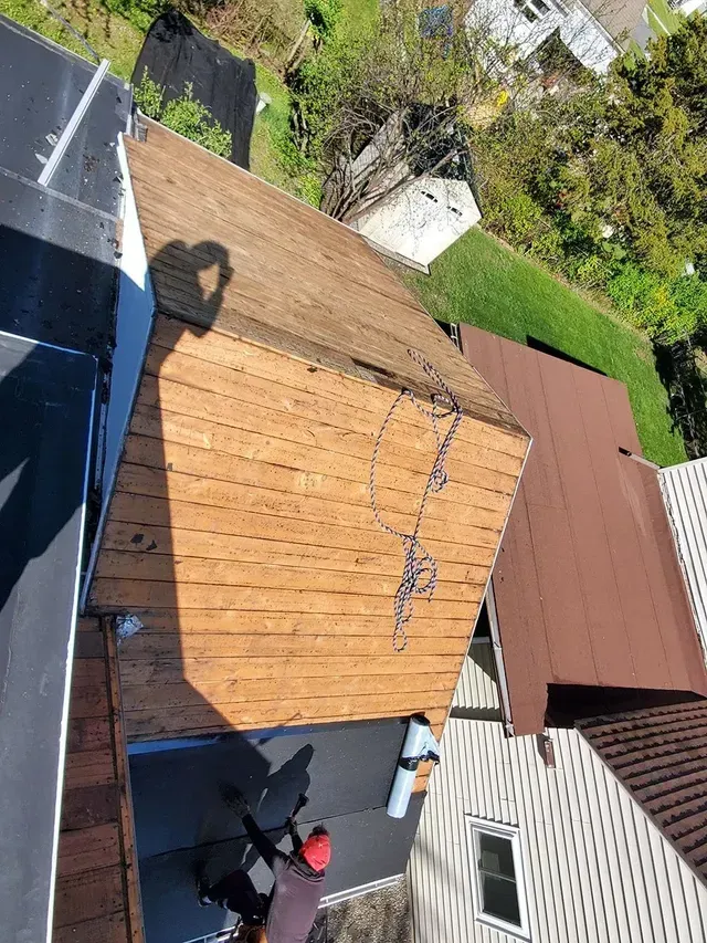 Overhead view of a roof with an attached shed and person working. Brown shingles and dark asphalt.