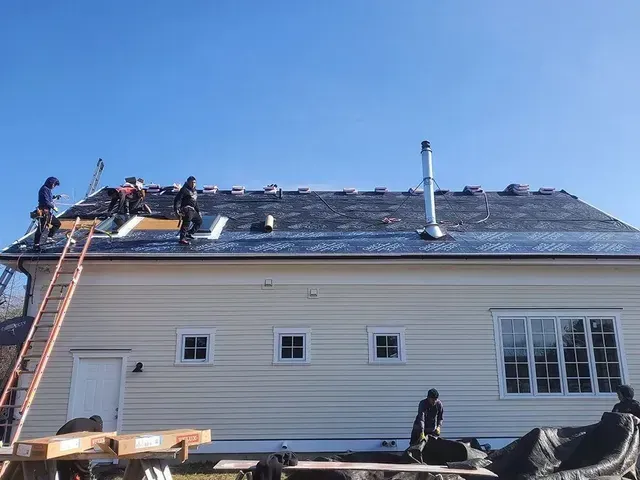 Roofers on a house with ladder, removing old shingles, preparing for new roof. Blue sky.