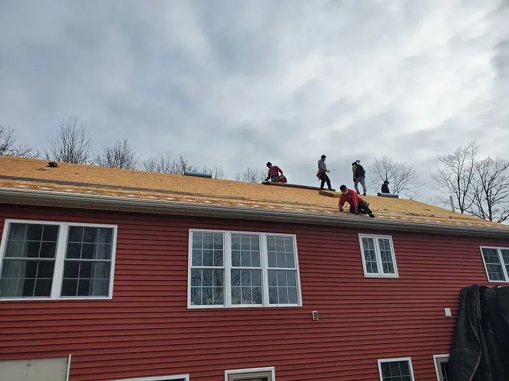 Roofers working on a red house roof under a cloudy sky.