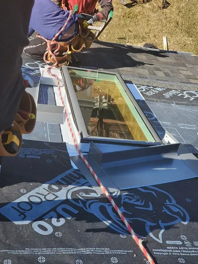 Roofer installing a skylight on a roof. Safety harness and rope visible.