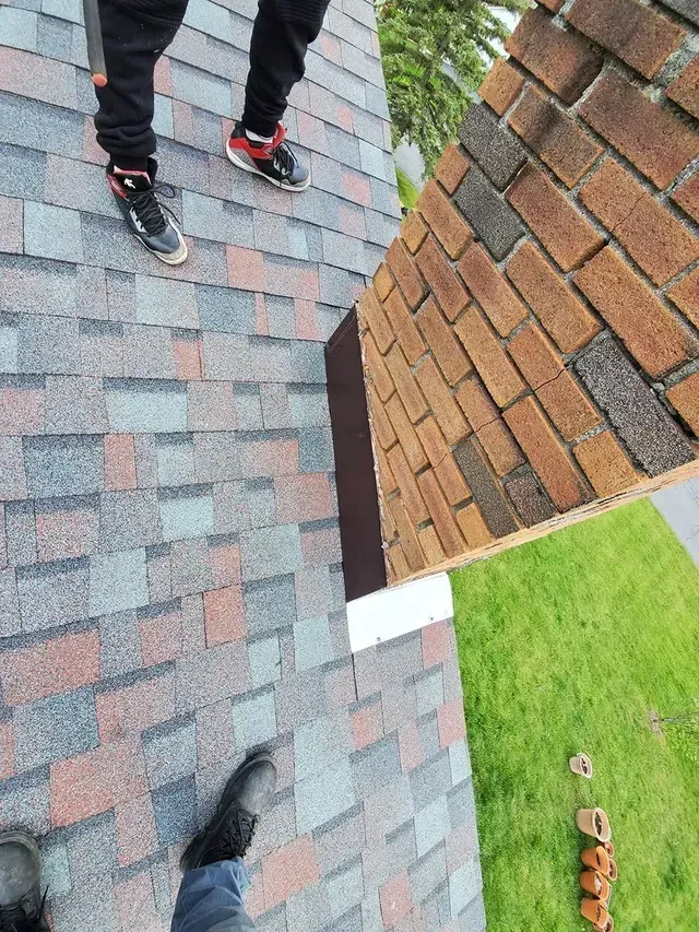 A person on a roof installing shingles. New and old shingles visible.