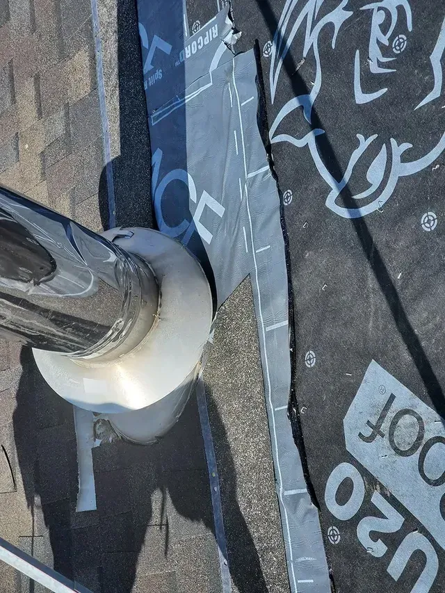 Close-up of a chimney flashing on a roof, surrounded by roofing materials and sealant.
