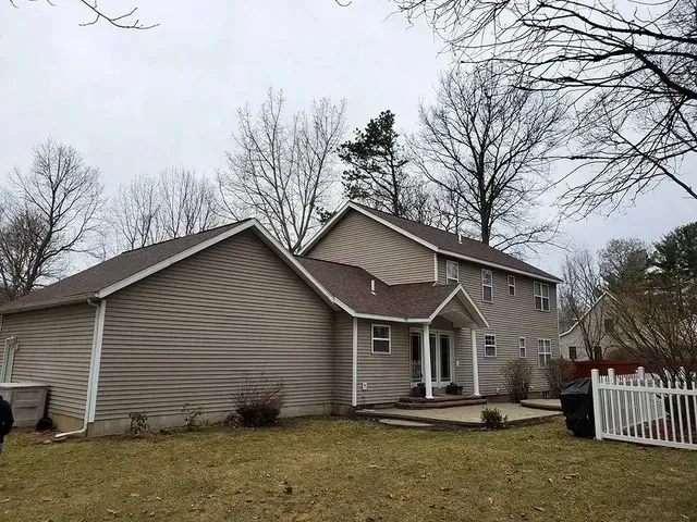 Tan two-story house with brown roof and siding on a cloudy day, viewed from backyard.