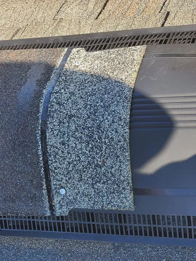 Close-up of a damaged asphalt shingle roof. One shingle is lifted, exposing underlayment.