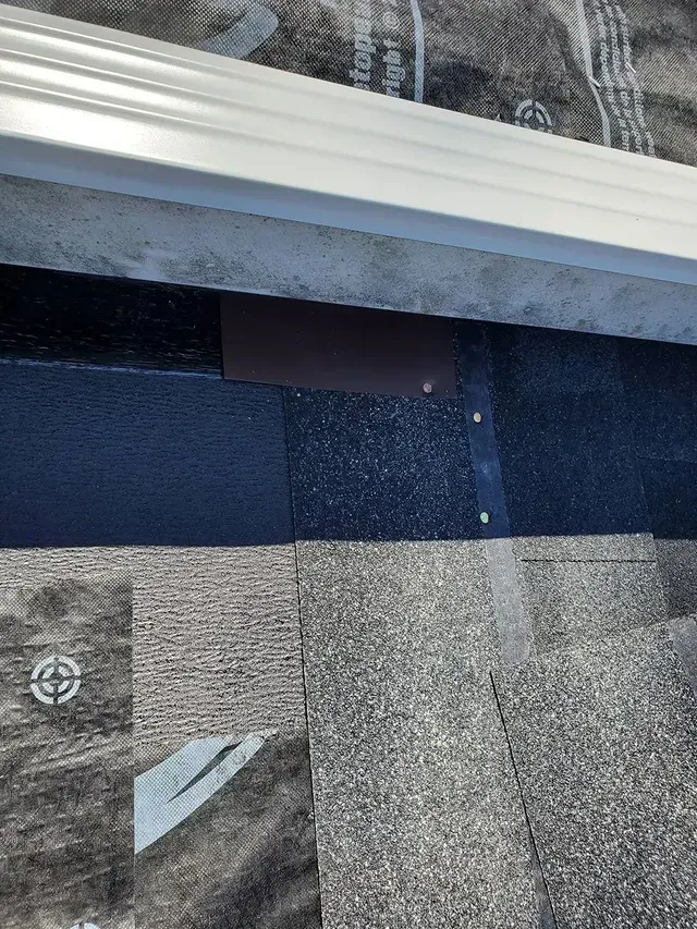 Roof shingles with flashing under a white gutter.